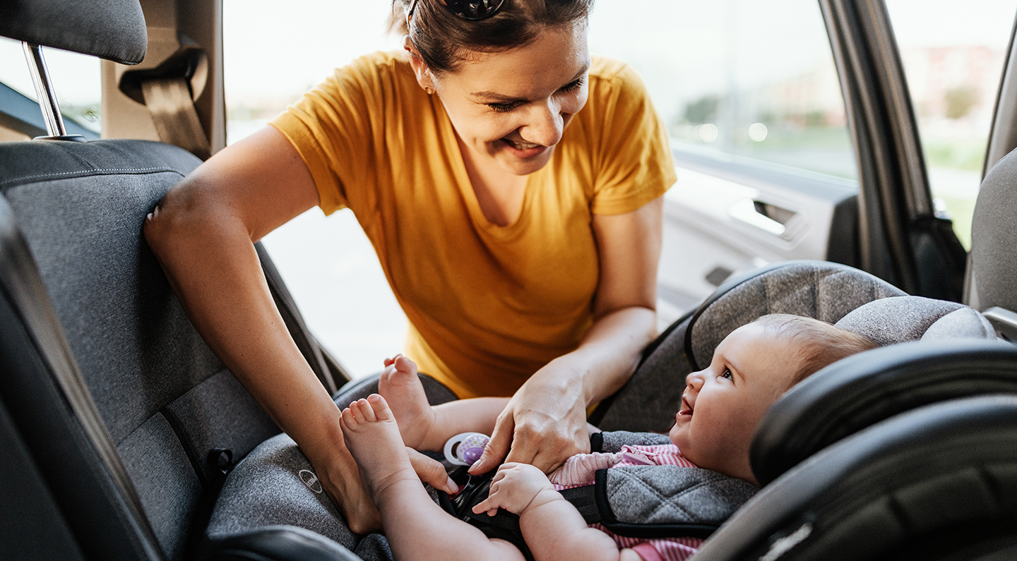 Photo of woman buckling her infant into a rear-facing infant car seat in the back seat of a vehicle