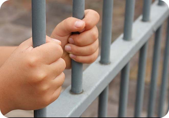 Photo of adult hands gripping jail cell bars